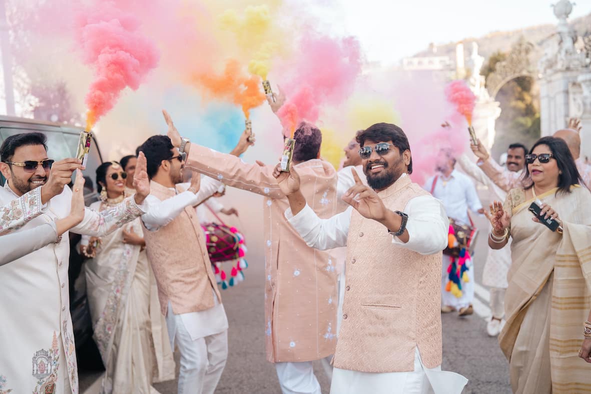 A group of Indian men dancing and waving coloured smoke flares. They are all wearing traditional Indian wedding clothes. Guests enjoying a lively Barat at an Indian wedding in Italy. Arranged by Love Italy Weddings, the best Indian wedding planner in Italy.