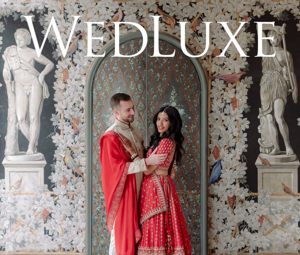 A couple embrace in front of a muraled wall at Villa Miani in Rome. They are wearing traditional Hindu outfits.