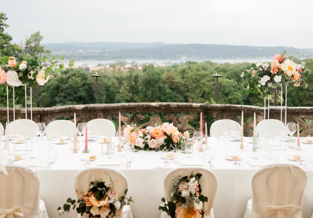 A beautifully set-up wedding table outside on a terrace. There is a view of Lake Maggiore in the background.