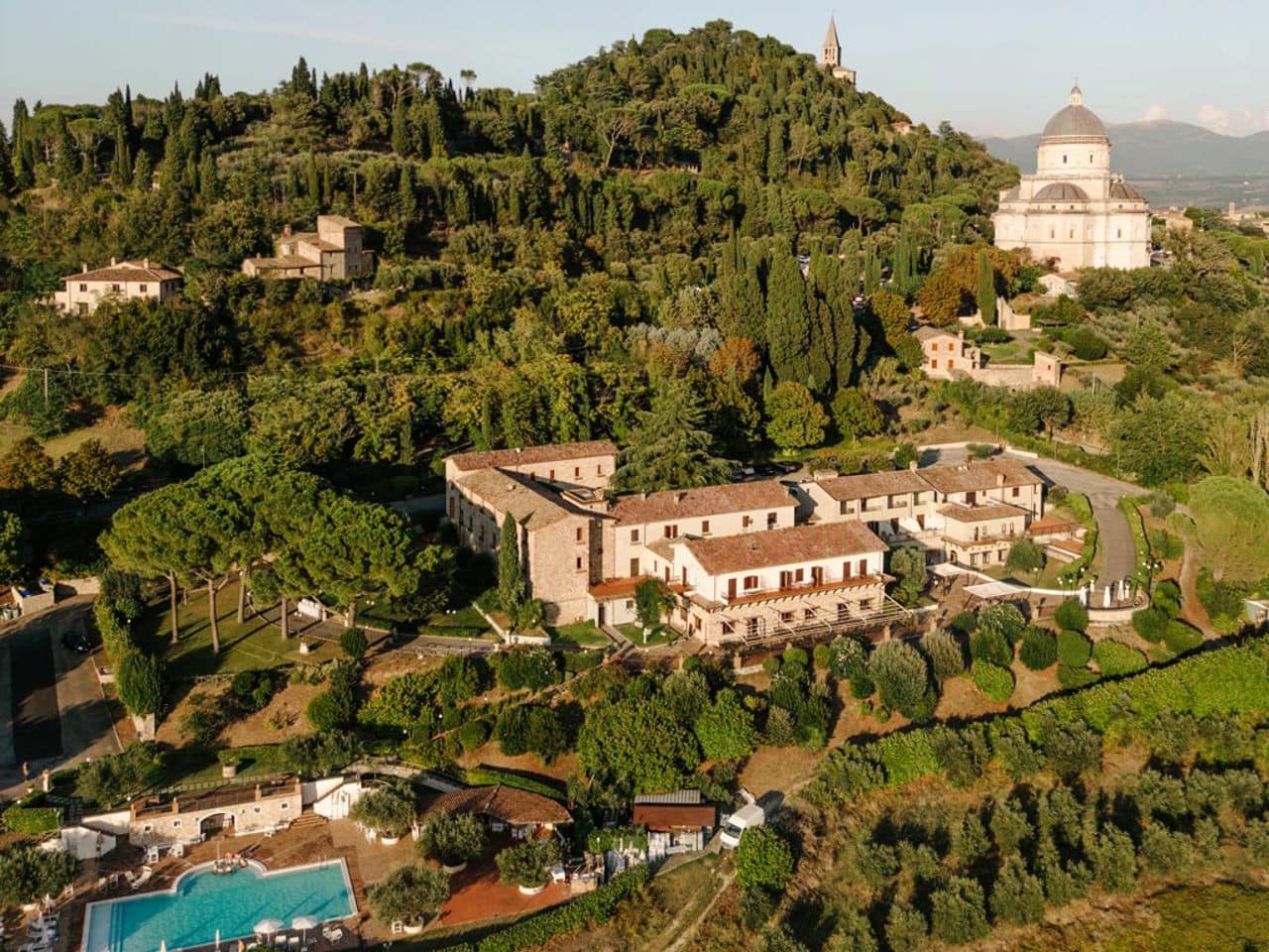 Aerial view of wedding venue in Todi, Umbria. There is a historic looking large building set on a green wood hillside.