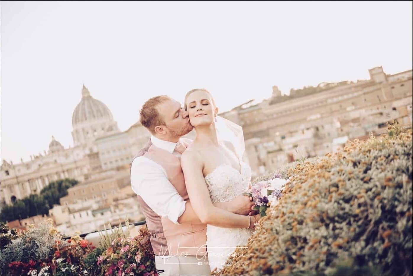 Newlyweds embrace on a rooftop in Rome. There is a view of the dome of St Peter's behind them-