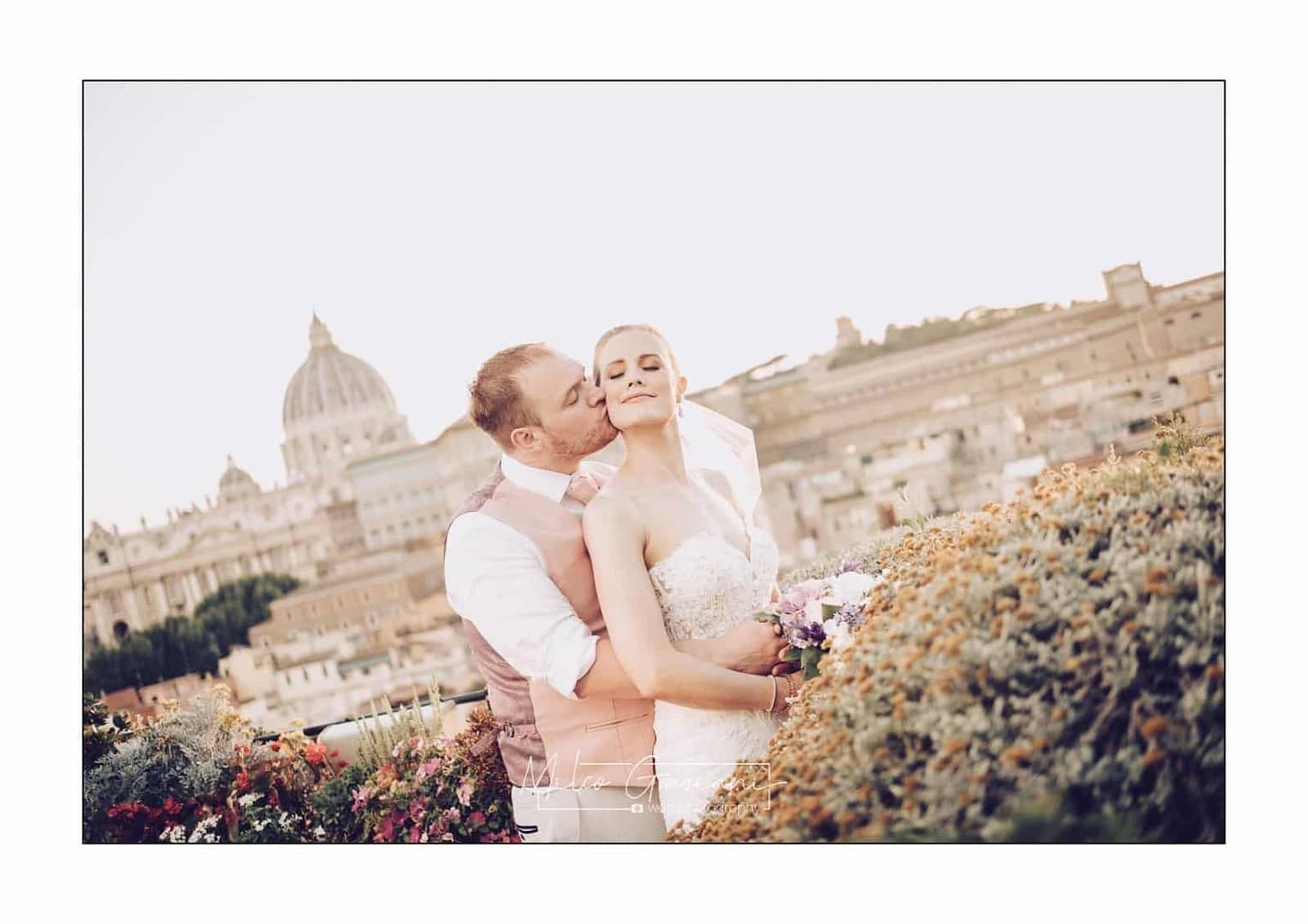 Newlyweds embrace on a rooftop in Rome. There is a view of the dome of St Peter's behind them-