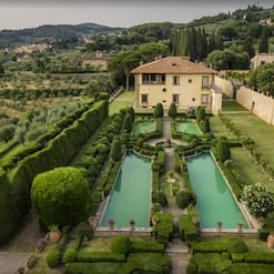 Italian villa with formal gardens. In front of the villa are four rectangular ponds with low hedges around them. There are lawns to the right of the ponds and olive groves to the left. The villa is at the back of the picture.