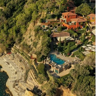 Hotel complex set on a wooded hillside leading down to the sea.  You see orange buildings and a swimming pool.