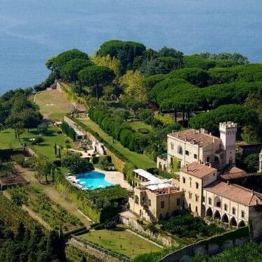 Aerial view of an antique palace wedding venue.  It is set in gardens with a swimming pool on a headland over the sea.