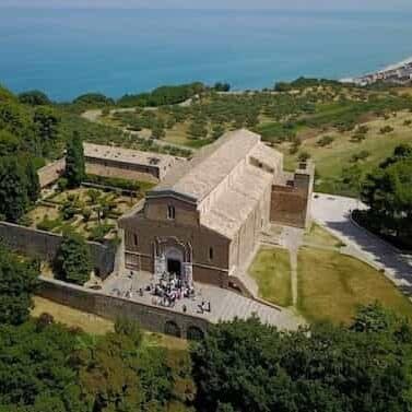 Aerial view of an abbey on a green hillside over the sea.