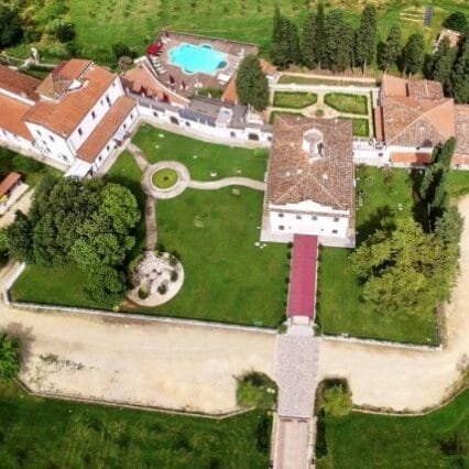 Aerial view of Villa Tolomei in Florence.  There is e lawn around the villa.  There are outbuildings also around the lawn and a swimming pool can be seen behind the villa.