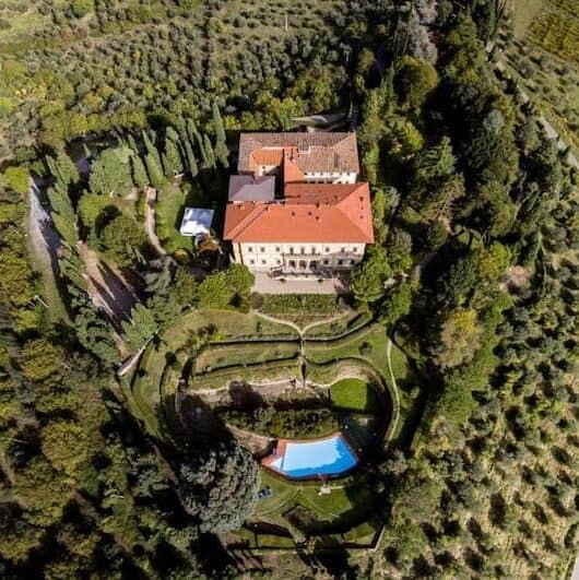 Tuscan villa with a large red roof photo from the air.  There are trees all around and a swimming pool in the front garden.