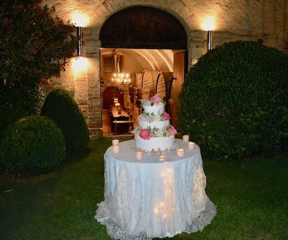 Wedding cake on a decorated table in front of very old open door. Inside the door you can see large wooden wine barrels. The setting is an historic vineyard, now converted into a luxury wedding venue.