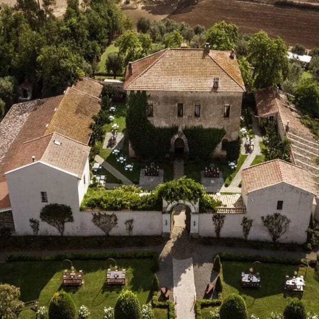 Rural Italian house with outbuildings in front creating a courtyard.  There are lawns and the house is partly covered by ivy.