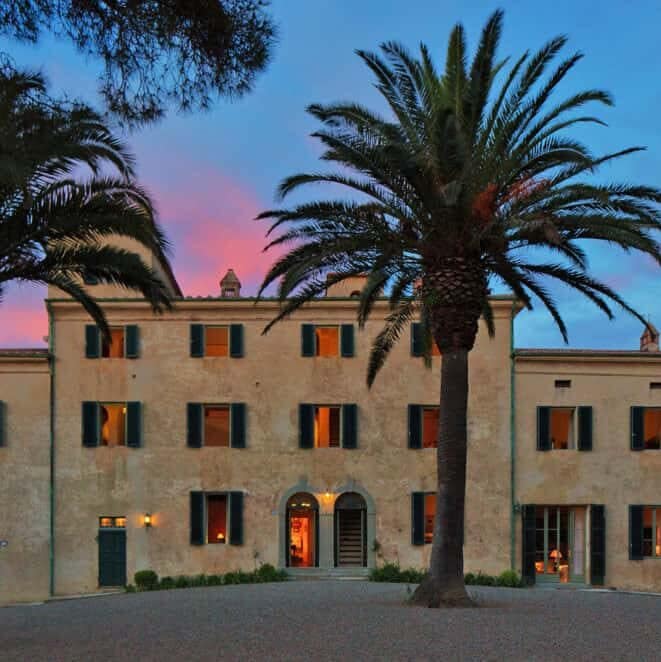 three storey Italian villa facade with a palm tree in front of it.