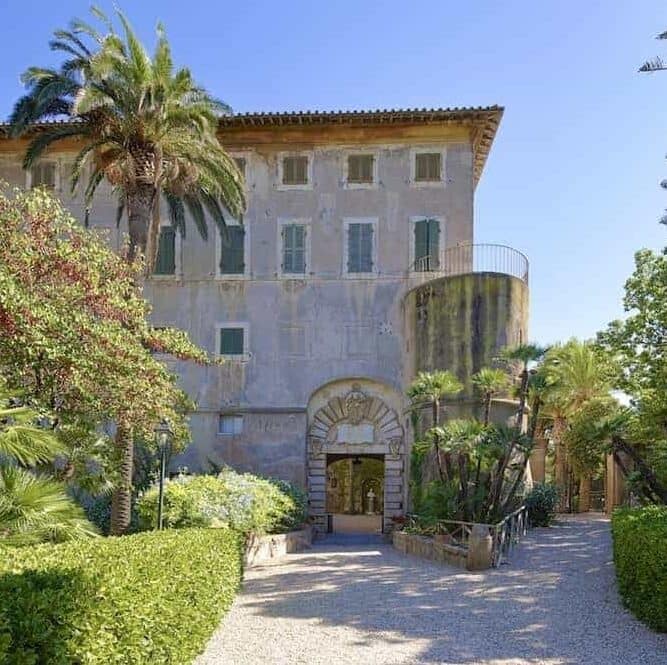 Frontal view of Italian antique villa.  Gardens in front with palm tree and gravel drive.