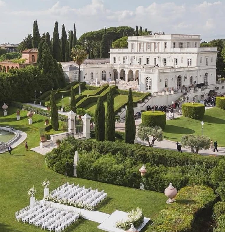 Aerial view of VILLA MIANI in Rome. There is a wedding set up with white flowers and chairs on the lawn in front of the villa.