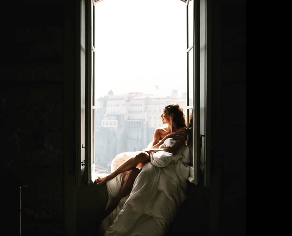 Relaxed bride at destination wedding in Italy looks out of antique window.